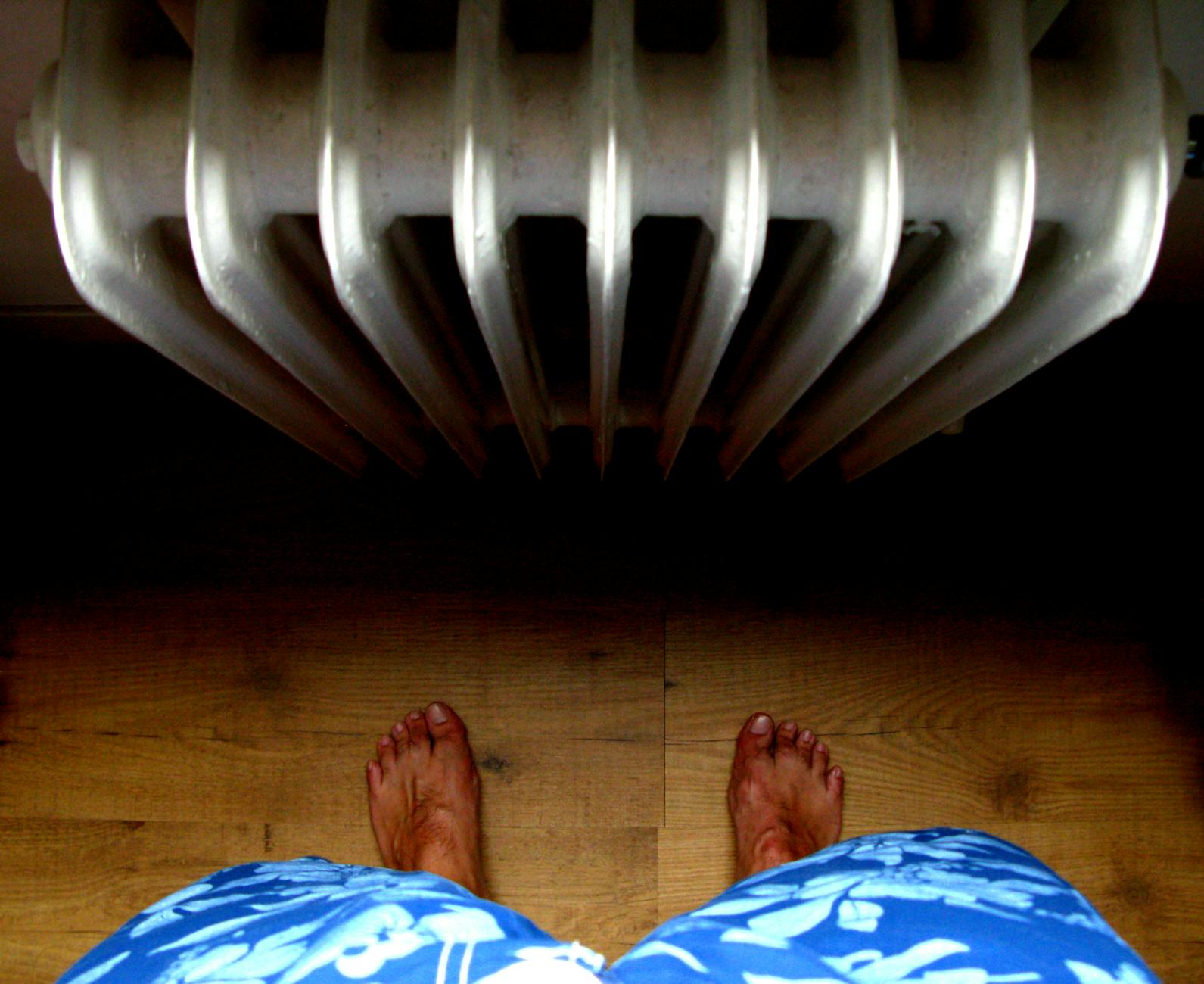 Stopy boso na drewnianej podłodze obok grzejnika w ogrzewanym domu