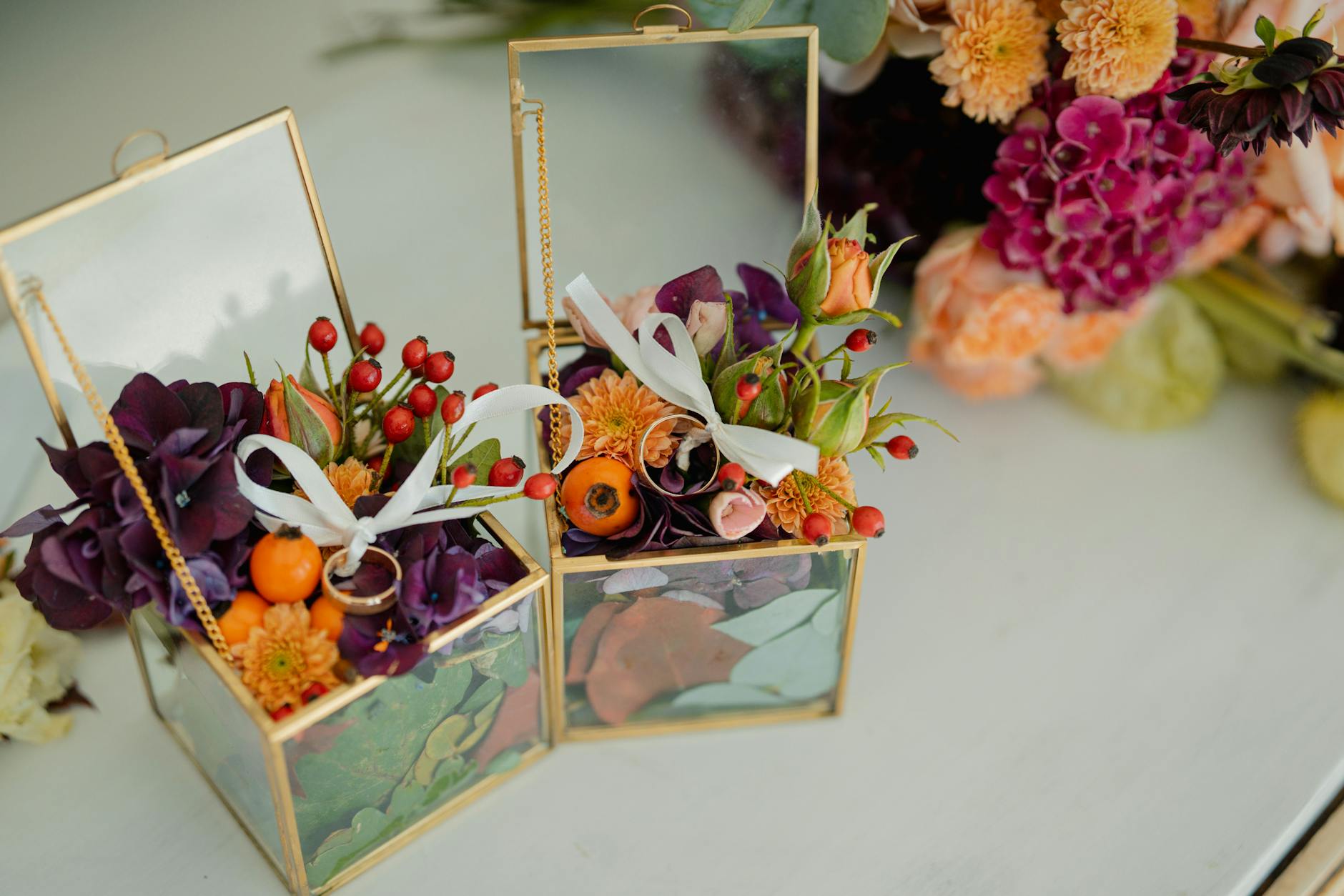 Szklane pudełka na obrączki wypełnione kwiatami i owocami na ślub