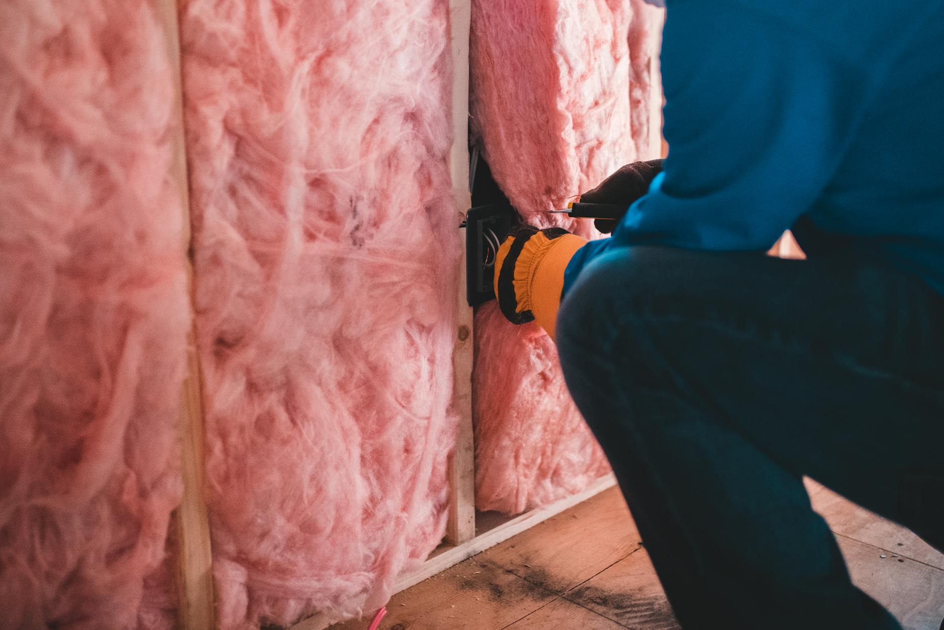 Pracownik w rękawicach montuje różową wełnę mineralną w ścianie
