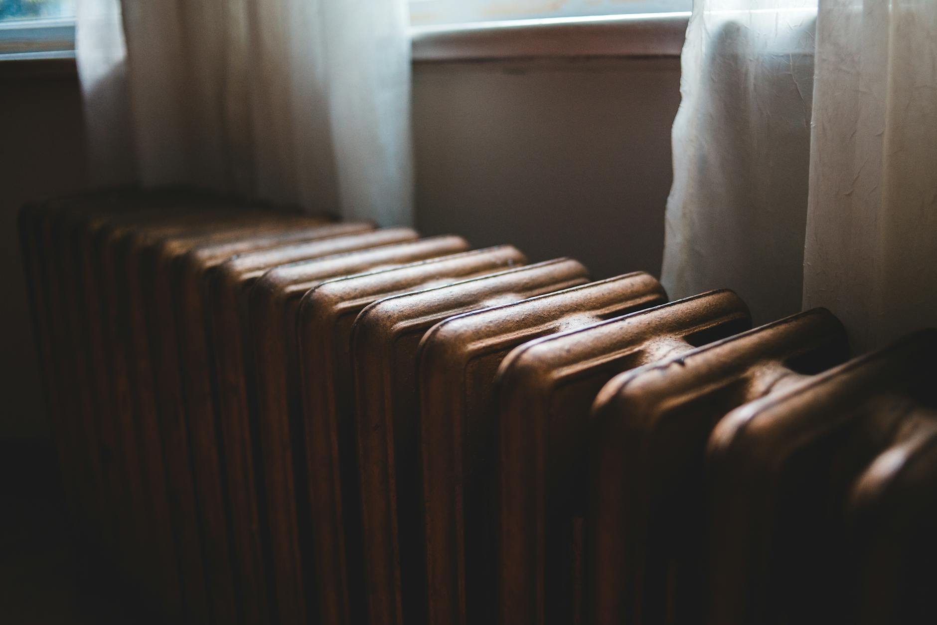 Żeliwny grzejnik pod oknem z firanką w mieszkaniu