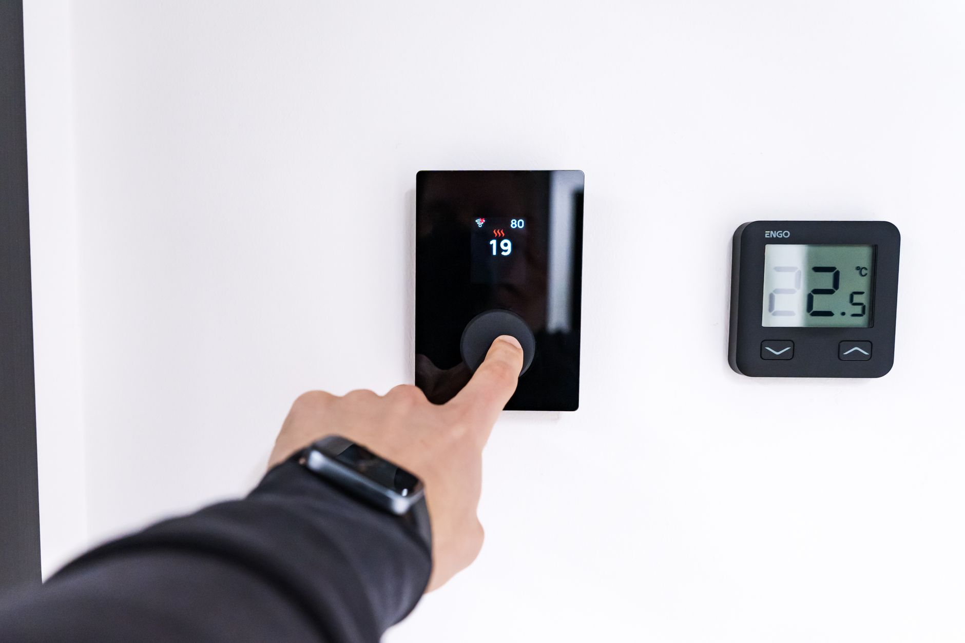 Smart home a ogrzewanie: co wybrać, żeby nie skończyć z chaosem Ręka ustawiająca cyfrowy termostat w nowoczesnym inteligentnym domu